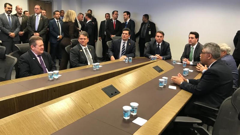 Mesa de reuniões em que se vê o presidente da República, Jair Bolsonaro, o ministro da Justiça e da Segurança Pública, Sergio Moro, além de outras autoridades.