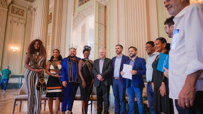 Grupo de carnavalescos e autoridades do Governo do Estado do Rio Grande do Sul reunidos em pé e posando para foto