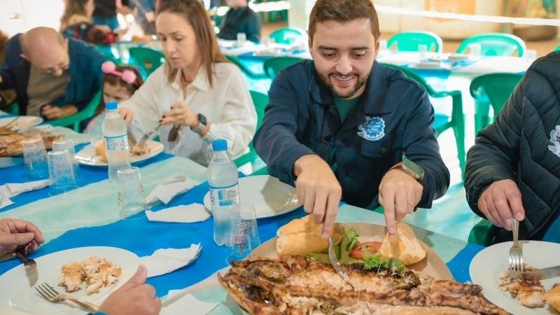 Governador em exercício está em uma mesa, ao lado da esposa e da filha, comendo a tainha assada