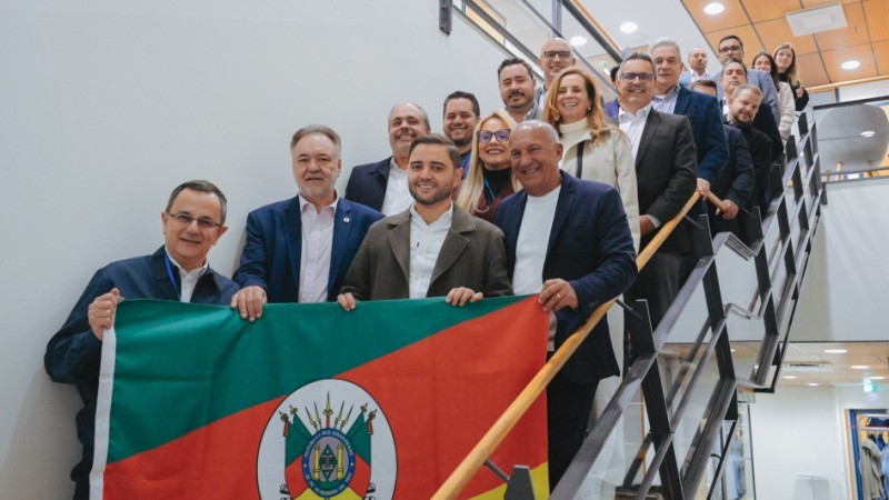 Comitiva que participou da missão pousa em uma escada, segurando a bandeira do Rio Grande do Sul.