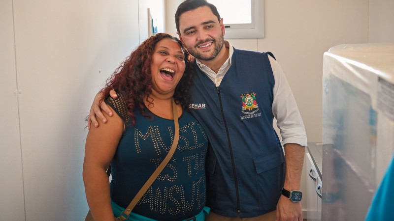 Gabriel Souza abraça uma mulher durante entrega de moradias temporárias. Ambos sorriem.