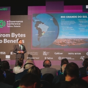 Gabriel Souza aparece de pé, na frente dos slides, diante do público da e-Gov Conference.