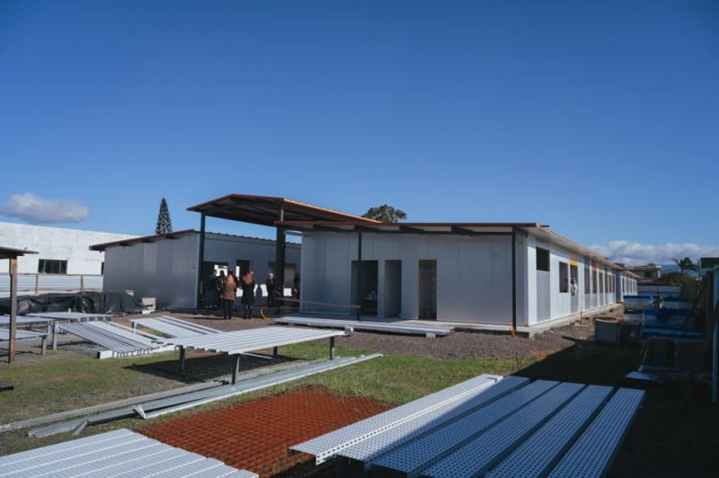 A imagem mostra o vice-governador Gabriel Souza vistoriando uma obra em uma escola. Ele está acompanhado por outras pessoas no canteiro de construção, onde estruturas metálicas e painéis indicam o uso de construção a seco. O cenário transmite um momento de inspeção e avanço em melhorias na infraestrutura educacional.